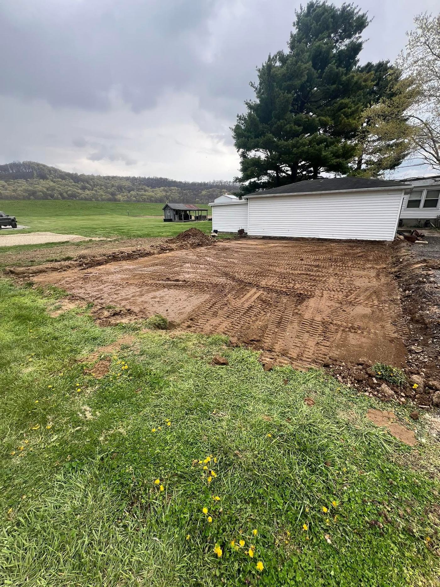 Graded dirt pad prepped beside a house, cleared and leveled with visible equipment tracks