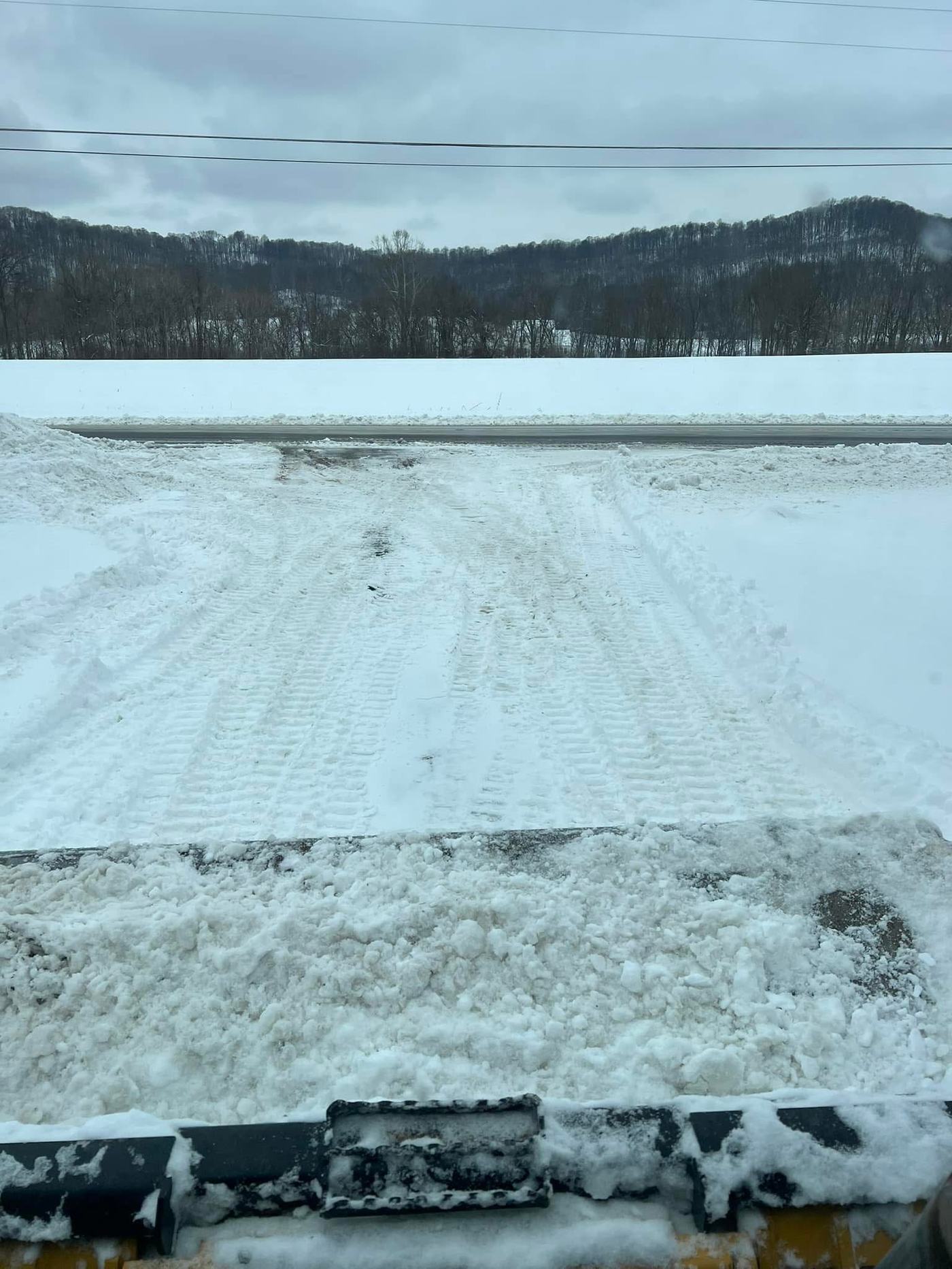 Snow-covered lane pushed clear down to gravel, viewed from behind a plow blade